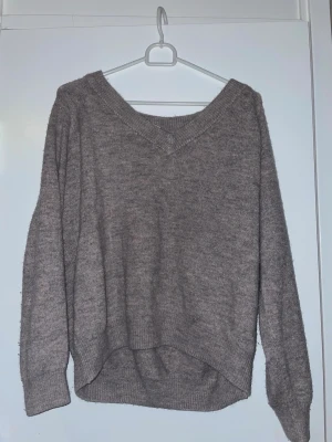 Grå stickad tröja med v-ringning - Mysig grå stickad tröja med v-ringad hals och långa ärmar. Tröjan har en avslappnad passform och ribbade muddar vid ärmslut och nederkant. Perfekt för lager på lager under kyliga dagar.