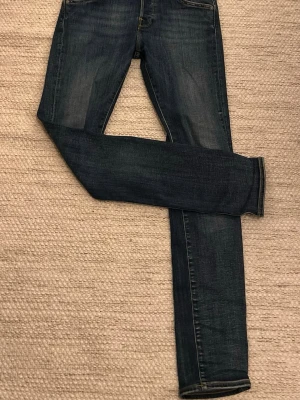 Mörkblå jeans från Jack & Jones - Säljer ett par mörkblå jeans från Jack & Jones med klassisk femficksdesign och snygga kontrastsömmar. Jeansen har en rak passform och är tillverkade i slitstarkt denimtyg. Perfekta för dig som gillar en enkel och tidlös look.
