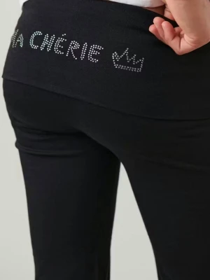 Svarta bootcut mjukisbyxor med strass - Säljer ett par svarta mjukisbyxor med bootcut passform och bred linning. På linningen bak står det 'MA CHÉRIE' i strass och en liten krona i strass. Byxorna är stretchiga och sköna, perfekta för en chill look. Jag har fått ett hål på baksidan men de är igensytt, syns knappt!!