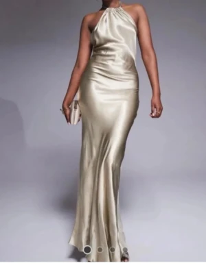 Champagnefärgad balklänning - Jättefin champagne/guldfärgad klänning i satin, perfekt till bal. Den är halterneck och öppen i ryggen. Storlek 36.