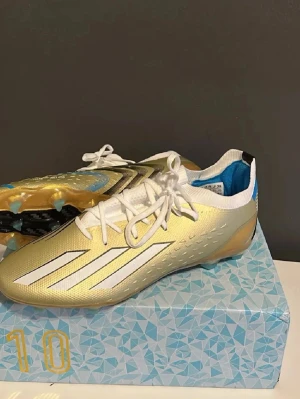 Adidas speedportal Messi (limited edition, nya) - Snygga fotbollsskor från Adidas i guld och vitt med svarta och blå detaljer. Skorna har snörning, låg profil och klassiska tre ränder på sidan. Ovandelen är i syntetmaterial och insidan är fodrad med blått tyg. Perfekta för dig som vill sticka ut på planen. Kan gå ner i pris vid snabb och smidig affär 