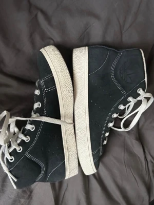 Svarta adidas sneakers i mocka - Säljer ett par svarta adidas sneakers i mocka, Mellanhöga och med gummisula i brunt. Perfekta för dig som gillar retrostil och streetwear.