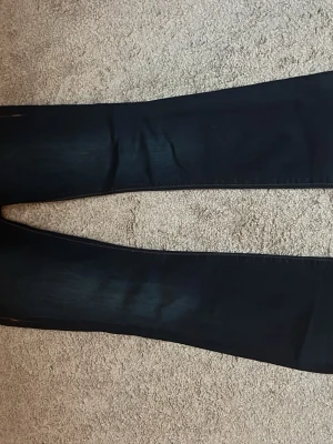 True Religion bootcut jeans mörkblå - Säljer ett par mörkblå jeans från True Religion med bootcut passform. Byxorna har kontrastsömmar, stora fickor bak med dekorativa knappar och tydlig logga på bakfickan. Klassisk jeanslook med snygga detaljer och markerade sömmar.