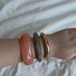 Snygga chunky armband i mixade färger - Fyra statement-armband i olika former och färger. Ett tjockt rosa armband med marmorerad look, ett grått marmorerat armband, samt två guldfärgade metallarmband med öppen design. Perfekt för att mixa och matcha till din outfit. Det smala guld färgade armbandet är till armen.