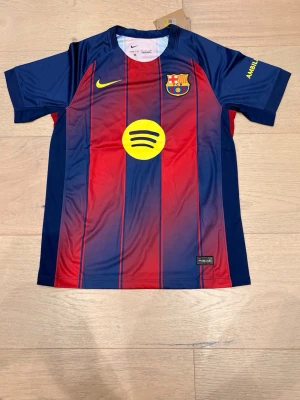 Barça matchtröja Lamine Yamal nr 10 - FC Barcelona matchtröja med Lamine Yamal och nummer 10 på ryggen. Tröjan är randig i marinblått och rött med gula detaljer och klubbmärke på bröstet. Tillverkad i polyester och har officiella sponsorer tryckta fram och bak.