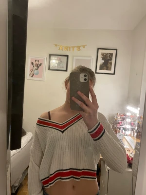 Stickad, kroppad tröja med v-neck - Säljer en stickad tröja med v-neck. Tröjan är kroppad och har ränder (röd och mörk blå/svart) för en touch av design. Perfekt för vinter, vår och höst (kan bli för varm på sommaren).