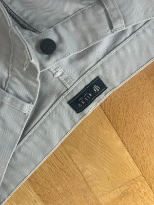 Ljusbeige raka byxor från Riley - Säljer ett par ljusbeige byxor från Riley i rak modell. Byxorna har klassisk femficksdesign, knapp och dragkedja framtill. Materialet är 55% bomull och 45% polyester vilket gör dem både mjuka och slitstarka. Perfekta till en clean och stilren look. Jeans.