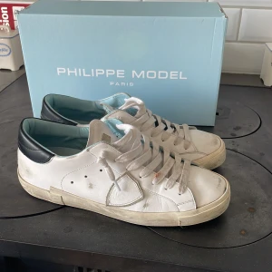 Vita Philippe Model sneakers i skinn - Snygga vita sneakers från Philippe Model i skinn med svarta detaljer på hälen och ljusblå insida. Klassisk låg modell med rund tå och vita snören. Perfekta för en clean och stilren look. Mycket fint skick, köpta för 4400