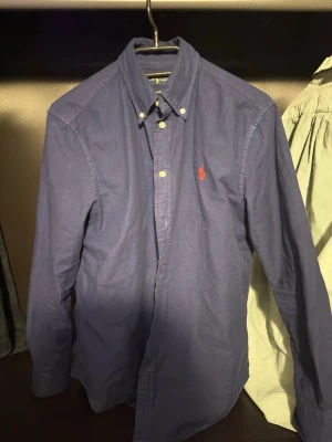 Blå skjorta från Ralph Lauren i S - Klassisk marinblå skjorta från Ralph Lauren i bomull med relaxed fit. Skjortan har knappar framtill, button-down krage och den ikoniska röda broderade loggan på bröstet. Långärmad och perfekt till en clean och stilren look.