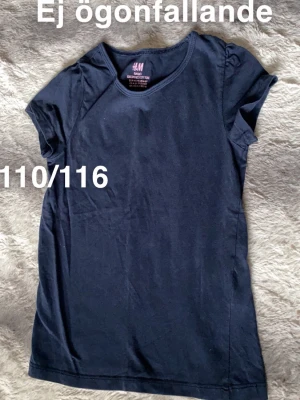 Marinblå t-shirt från H&M barn - En enkel marinblå t-shirt från H&M. Klassisk rund halsringning och korta ärmar med lätt puff vid axlarna för en söt touch. Perfekt basplagg till garderoben.🌸 Ojämn i färgen. Storlek 110/116