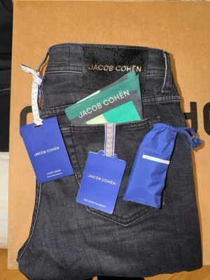 Jacob Cohën jeans i nyskick - Säljer ett par Jacob Cohen jeans i storlek 31, modell Bard. Svarta med stilren badge. Jeansen är i nyskick och har alla lappar och tilläggningar kvar – inga tecken på användning. Nypris: 5799kr. Digitalt kvitto tillgängligt. 