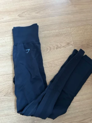 Mörkblå Gymshark leggings - Säljer ett par mörkblå flex leggings från Gymshark med hög midja och bred resår där loggan syns tydligt baktill. Använda sparsamt då dem är för små för mig nu
