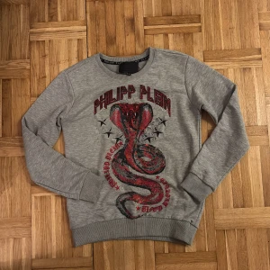 Grå sweatshirt Philipp Plein S - Grå sweatshirt från Philipp Plein med ett stort tryck av en röd och svart orm på framsidan och dekorerad logotyp i rött. Rund hals, ribbade muddar och långärmad. Snygg streetstil med coola detaljer och print.