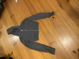 Mörkgrå hoodiejacka från H&M Divided - Säljer en mörkgrå hoodiejacka från H&M Divided i storlek XXS. Jackan har dragkedja framtill, huva och ribbade muddar vid ärmslut och nederkant. Perfekt för chill dagar och enkel att matcha med jeans eller leggings.