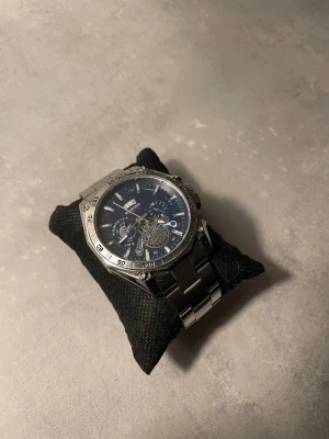 Binbond silverfärgad kronografklocka - Snygg kronografklocka från Binbond med robust silverfärgat armband i metall och blå urtavla med flera funktioner. Klockan har tachymeter på ringen, datumvisning och synliga mekaniska detaljer. Perfekt för dig som gillar detaljer och teknisk design.