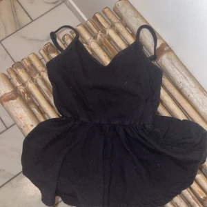 Svart kort klänning från SHEIN Teen - Supersöt svart klänning från SHEIN Teen med smala axelband och v-ringad hals. Kjolen är lätt utställd och tyget har en diskret ribbad struktur. Perfekt för dig som gillar enkel och stilren look med en touch av edge.