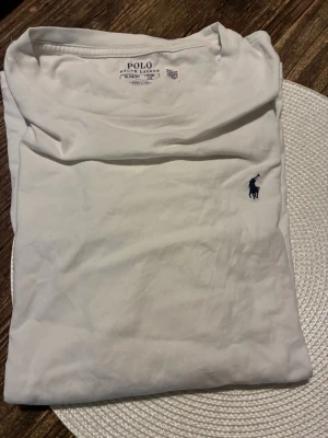 Vit t-shirt från Polo Ralph Lauren XL - Vit t-shirt från Polo Ralph Lauren i storlek XL. Klassisk design med korta ärmar och den ikoniska broderade loggan i marinblått på bröstet. Tillverkad i mjuk bomull för skön känsla och stilren look.
