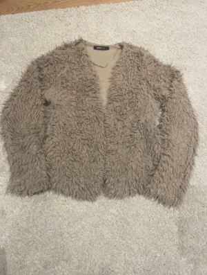 Beige pälsjacka från Gina Tricot - Säljer en fluffig och mysig beige pälsjacka från Gina Tricot i storlek S. Jackan har långärmade ärmar och en loose passform, perfekt för dig som gillar en chill och trendig look. Den har en öppen framsida utan knappar eller dragkedja.