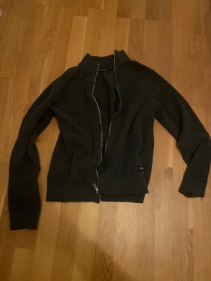  Jack & Jones fullzip  - Snygg mörkgrå kofta från Jack & Jones med hel dragkedja framtill och ribbade muddar. Tröjan har en enkel, stilren design och är tillverkad i mjukt stickat material som passar perfekt för kyliga dagar. Perfekt att slänga på sig över en t-shirt. Tröjan är i xs men passar s också 