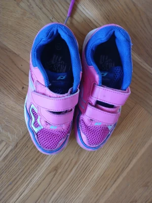 Rosa sneakers med kardborreband - Säljer ett par färgglada sneakers från Pro Touch i rosa med blå detaljer och vita sulor. Skorna har två praktiska kardborreband och meshpartier framtill för extra ventilation. Perfekta för dig som vill ha bekväma och snygga skor till vardagen.
