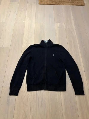 Full zip Polo ralph lauren  - Säljer en mörkblå zip-tröja från Polo Ralph Lauren med hög krage och dragkedja. Tröjan är stickad och har två fickor framtill. Perfekt för vardag och kyligare dagar med en klassisk, sportig look. Passformen är normal och tröjan är i 10/10 skick och sparsamt använd. Tveka inte att skriva vid frågor! 
