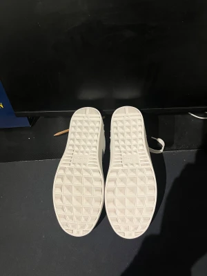 Valentino Garavani Open sneakers - Snygga Valentino Garavani Open sneakers i vitt skinn med en bred svart läderpanel över snörningen. Skorna har platt sula, rund tå och coola nitar på hälen för extra edge. Perfekt för dig som gillar exklusiv streetstil och vill sticka ut.