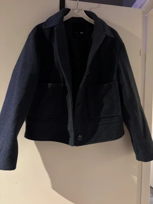 Mörkblå overshirt från 157, XS - Snygg mörkblå kappa  från 157 i storlek XS. Jackan har två stora fickor framtill, klassisk krage och stängs med knappar. Materialet är ullblandning som ger en mjuk och varm känsla, 