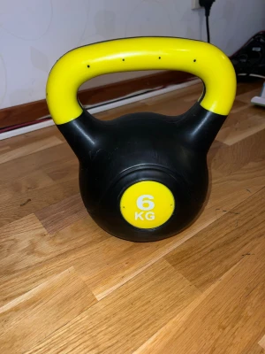 Kettlebell 6 kg - Kettlebell på 6 kg i svart och gult. Handtaget är ergonomiskt och lätt att greppa. Produkten har några ytliga repor och märken, men är i fullt fungerande skick. Perfekt för styrketräning hemma eller på gymmet.