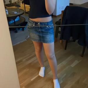 Blå jeanskjol från Gina tricot  - Säljer en blå jeanskjol från Vero Moda i kort modell med rå kant och slitningar. Kjolen har klassiska fickor fram och bak, bälteshällor och knappstängning. Perfekt för dig som gillar en chill och trendig denimlook.