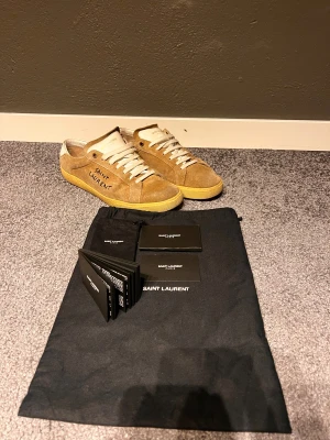 Saint Laurent skor - Snygga sneakers från Saint Laurent i brun mocka med vita detaljer och snörning. Skorna har rund tå, platt sula och Saint Laurent-logga på sidan och plösen. Medföljer originalpåse och äkthetskort. Perfekta för dig som gillar exklusiva och stilrena sneakers.
