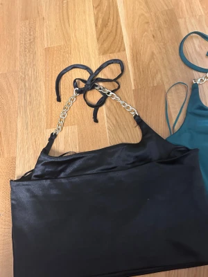 Satinlinne med guldkedjor - Två stilrena linnen i satin, ett svart och ett mörkgrönt. Båda har tunna axelband i guldfärgad kedja och knytning i nacken för en snygg detalj. Båda är storlek S. 60kr styck använda en gång 