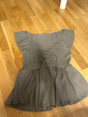 Grå blus med knyt och volang - Supersöt grå blus med v-ringning, knyt framtill och volangdetaljer. Storlek S aldrig använt 