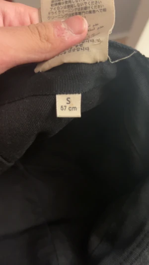 Svart keps från Gucci med läderdetaljer - Säljer en svart keps från Gucci med klassiska gröna och röda ränder på sidan. Kepsen har justerbart spänne i svart läder baktill och diskret GG-mönster i tyget. Materialet är bomull och läder, perfekt för dig som vill ha en stilren och lyxig accessoar.