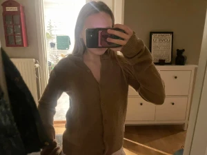 Beige stickad kofta med knappar - Mysig brun stickad kofta med långa ärmar och knappar framtill. Koftan har en klassisk rund halsringning och är perfekt för lager-på-lager. Den stickade strukturen ger en skön och avslappnad känsla, och färgen är lätt att matcha med det mesta.