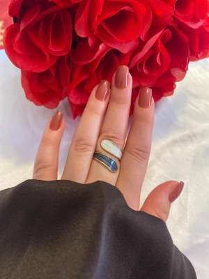 Unik guldpläterad statementring - Säljer en snygg och modern ring med två droppformade stenar i vitt och mörkblått, infattade i guldpläterad metall. Ringen har en öppen design som ger en cool och trendig look. Perfekt för dig som vill sticka ut med dina accessoarer.