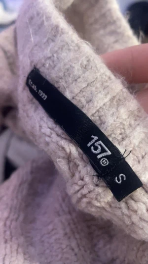 Ljusbeige stickad tröja från 157 - Supermysig ljusbeige stickad tröja från 157 med flätstickat mönster och ribbade muddar. Croppad modell som sitter snyggt och har långärmade ärmar. Perfekt för att hålla sig varm och ändå se chill ut.