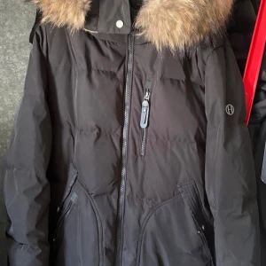 Svart dunjacka med päls från Hollies - Säljer en svart dunjacka från Hollies med fluffig päls runt kragen. Jackan har dragkedja framtill, flera fickor. Storlek 50 5 xl lite mindre i storleken. Nu pris 6000 kr säljes för 1600