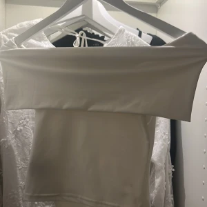 Vit axelbandslös tubtopp - Säljer en stilren vit tubtopp med axelbandslös design. Toppen har en rak, croppad passform och är sydd i ett stretchigt, mjukt material som sitter snyggt mot kroppen. Perfekt att matcha med jeans eller kjol för en clean look.