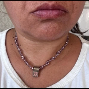 Rosa pärlhalsband från Othmar - Unikt halsband från Othmar København med rosa  pärlor och ett silverfärgat hänge. Halsbandet har dubbla rader av glansiga pärlor och ett rektangulärt hänge med lila stenar. Perfekt för dig som gillar färg och vill sticka ut.