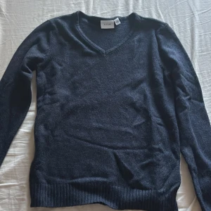 Mörkblå stickad tröja från Vila - Mysig mörkblå stickad tröja från Vila med v-ringad hals och långa ärmar. Tröjan har ribbade muddar vid ärmslut och nederkant, perfekt för lager på lager under kyliga dagar.