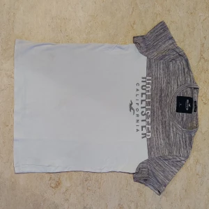 Vit och grå t-shirt Hollister XS - Snygg t-shirt från Hollister i storlek XS. Överdelen och ärmarna är gråmelerade medan resten av tröjan är vit. Tryck med 'Hollister California' framtill. Rund hals och korta ärmar. Tillverkad i 100% bomull för skön känsla.