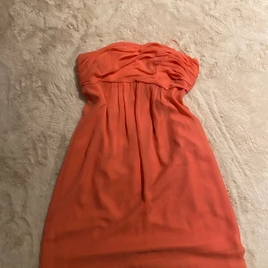 Cocktail klänning - Säljer en snygg korallfärgad axelbandslös klänning från Esprit Collection. Klänningen har draperad överdel, lätt veckad kjol och dragkedja i sidan. Materialet är tunt och luftigt, perfekt för varmare dagar. Stilren och feminin look och använt 2 ggr.