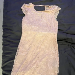 Ljusrosa spetsklänning från Vero Moda - Supersöt ljusrosa kortklänning från Vero Moda med v-ringning där bak och vackert spetsmönster. Klänningen har små ärmar och är figurnära med en feminin siluett. Perfekt för dig som vill ha en romantisk och elegant look.