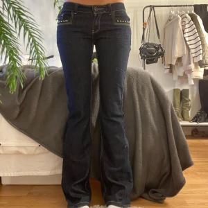Low Waist Bootcut jeans Royal Collection mörkblå - Mörkblå, låg midja, bootcut jeans från Royal Collection pärldetaljer på fickorna fram samt ett hjärta i paljetter på bakfickan. 