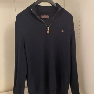 Mörkblå merinoullströja från Morris M - Snygg mörkblå stickad tröja från Morris i 100% merinoull. Tröjan har half zip-dragkedja med läderdetalj och diskret logga på bröstet. Perfekt för dig som gillar klassisk och stilren look med hög komfort. Tröjan har krymp i tvätten och är som strl M istället för XL men är fortfarande väldigt bra skick.                                                   Nypris 1799kr