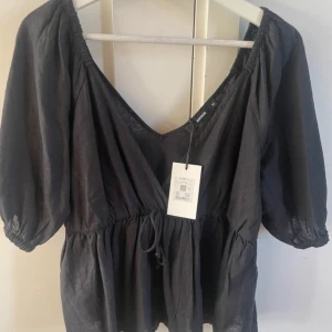 Svart blus med puffärm Bik Bok - Svart blus från Bik Bok . Toppen har v-ringning, puffiga trekvartsärmar med resår och en luftig, lätt struktur. Perfekt för dig som gillar en trendig och avslappnad look.