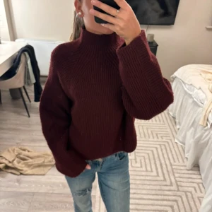 Vinröd stickad polotröja - Mysig vinröd stickad polotröja med hög hals och breda ärmar. Tröjan har en loose fit och är perfekt för kyliga dagar. Snyggt ribbstickat mönster som ger en trendig vibe. Passar grymt till jeans eller kjol.