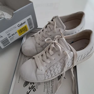 Vita sneakers från Gabor i skinn - Snygga vita sneakers från Gabor i skinn med flätad detalj på sidorna. Klassisk rund tå, platt sula och snörning framtill. Perfekta för dig som gillar stilrena och bekväma skor med en twist. Kommer i originalkartong.