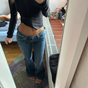 Blå bootcut jeans med broderade fickor - Säljer ett par blå bootcut jeans med låg midja och snygga broderade bakfickor med detaljer i beige och silver. 