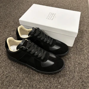 Svarta sneakers - Maison Margiela sneakers i svart skinn och mocka med svarta snören och kontrasterande vit insida. Klassisk låg modell och jätte fina skor Skriv gärna om intresserad 